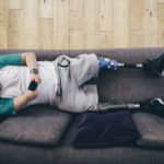 Quadriplegic man lying on the sofa at home. He is using a smartphone.